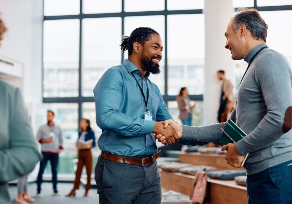 Happy black entrepreneur handshaking with a colleague while attending business conference at convention center.